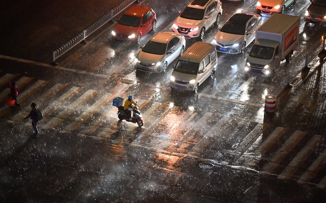 在天津市南开区，外卖骑手在风雨中骑行过马路。新华社资料